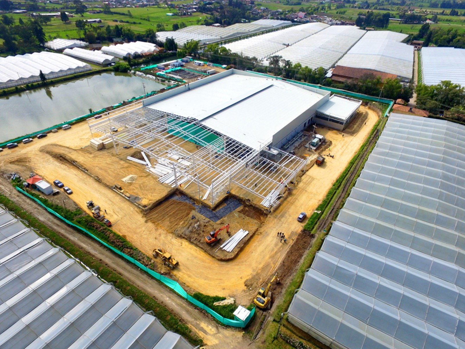 Vista aérea de bodega industrial en construcción rodeada de invernaderos