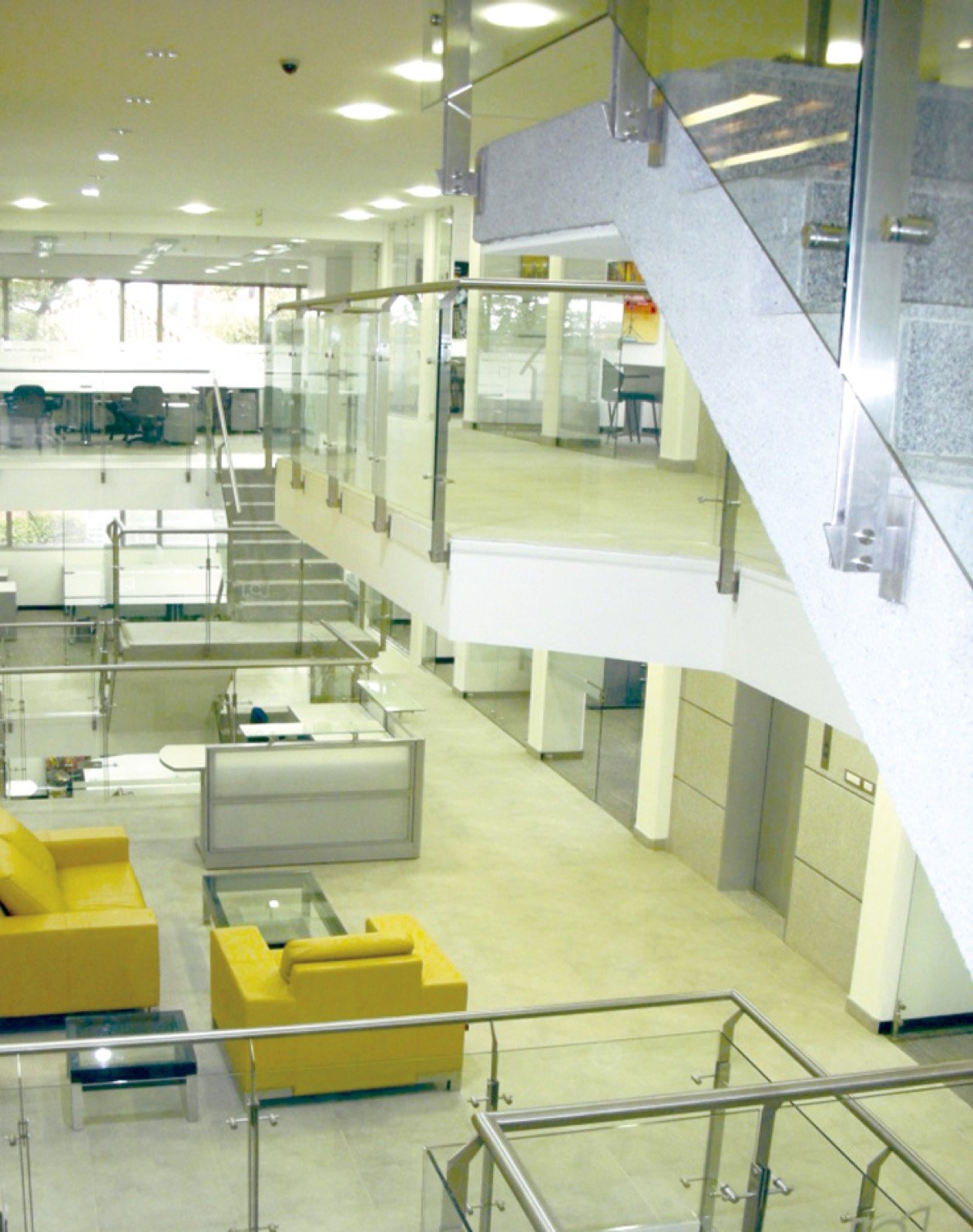 Interior de edificio corporativo con doble altura, barandas de vidrio y mobiliario